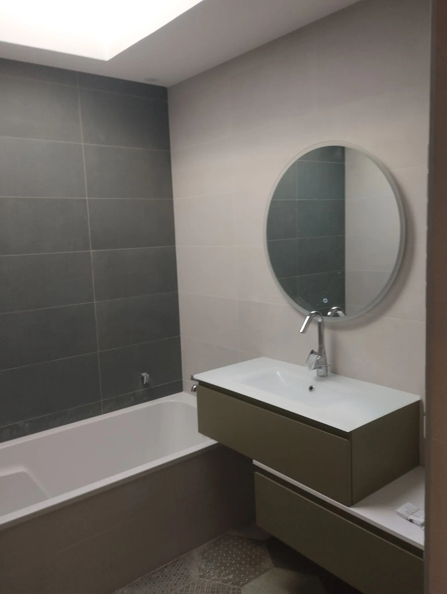 Salle de bain rénovée par EGM : faïence grand format, mur anthracite, baignoire et meuble suspendu